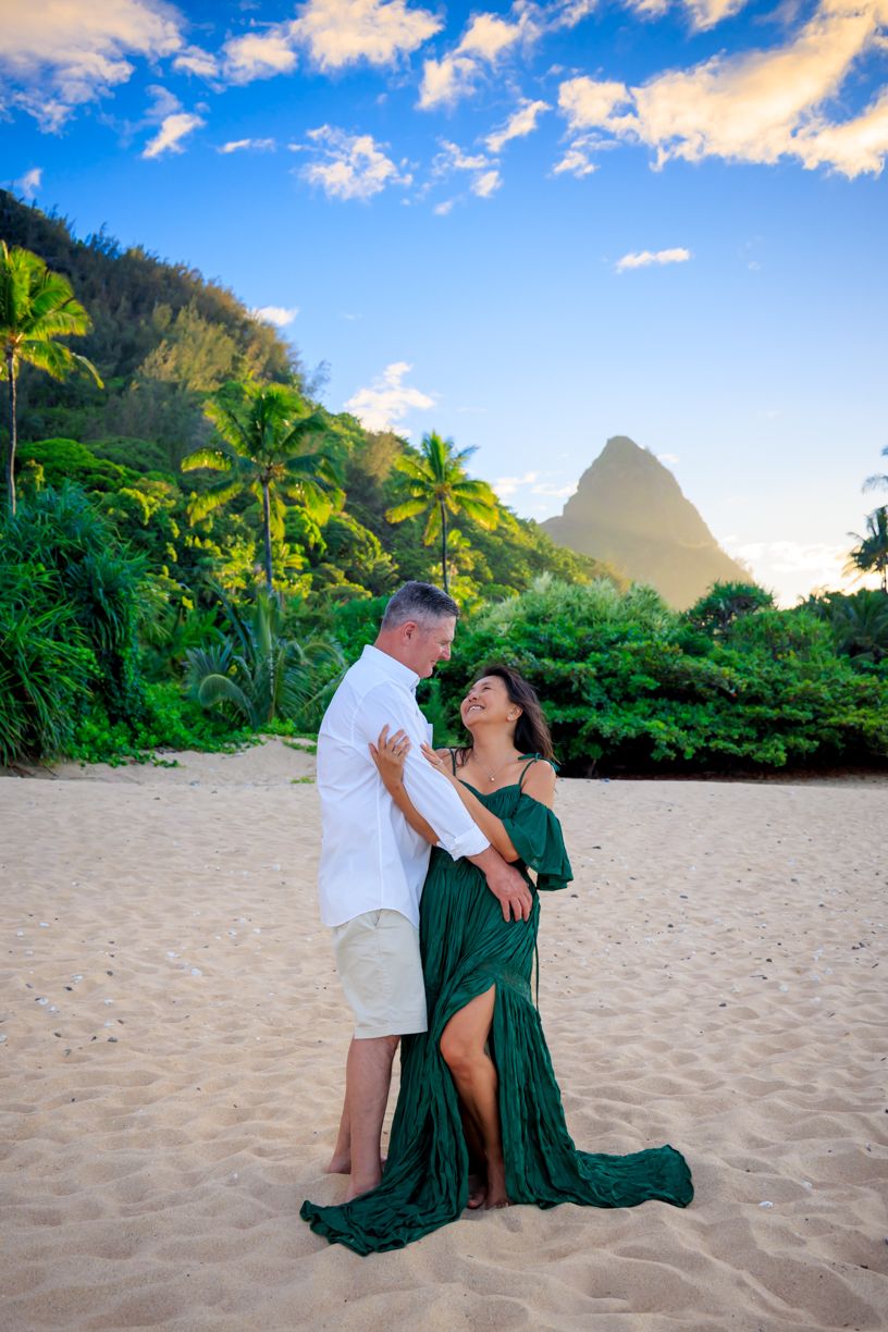 A romantic beach photoshoot at sunset with palm trees and mountains in Hawaii.