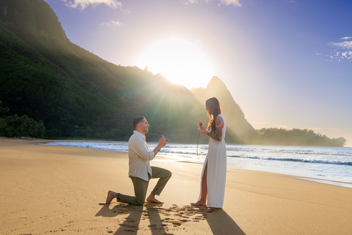 A proposal silhouette against a dramatic sunset on a Hawaiian beach with mountains.