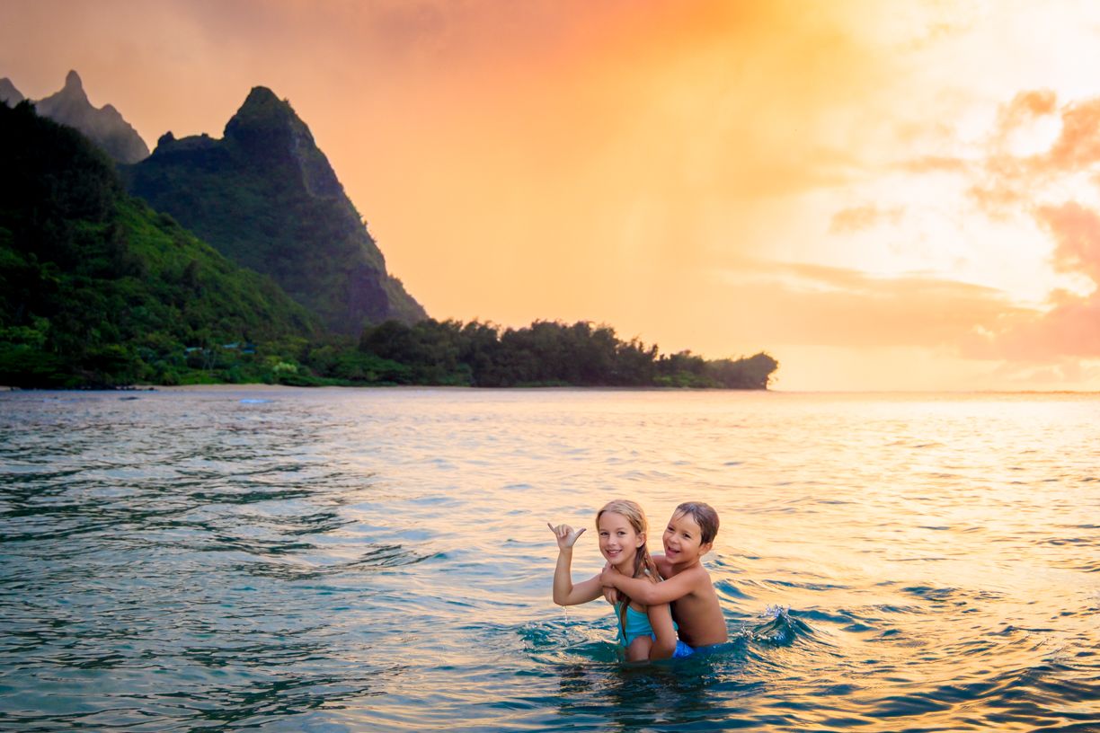 Group walking along a scenic beach at sunset with dramatic mountain silhouettes and orange sky.