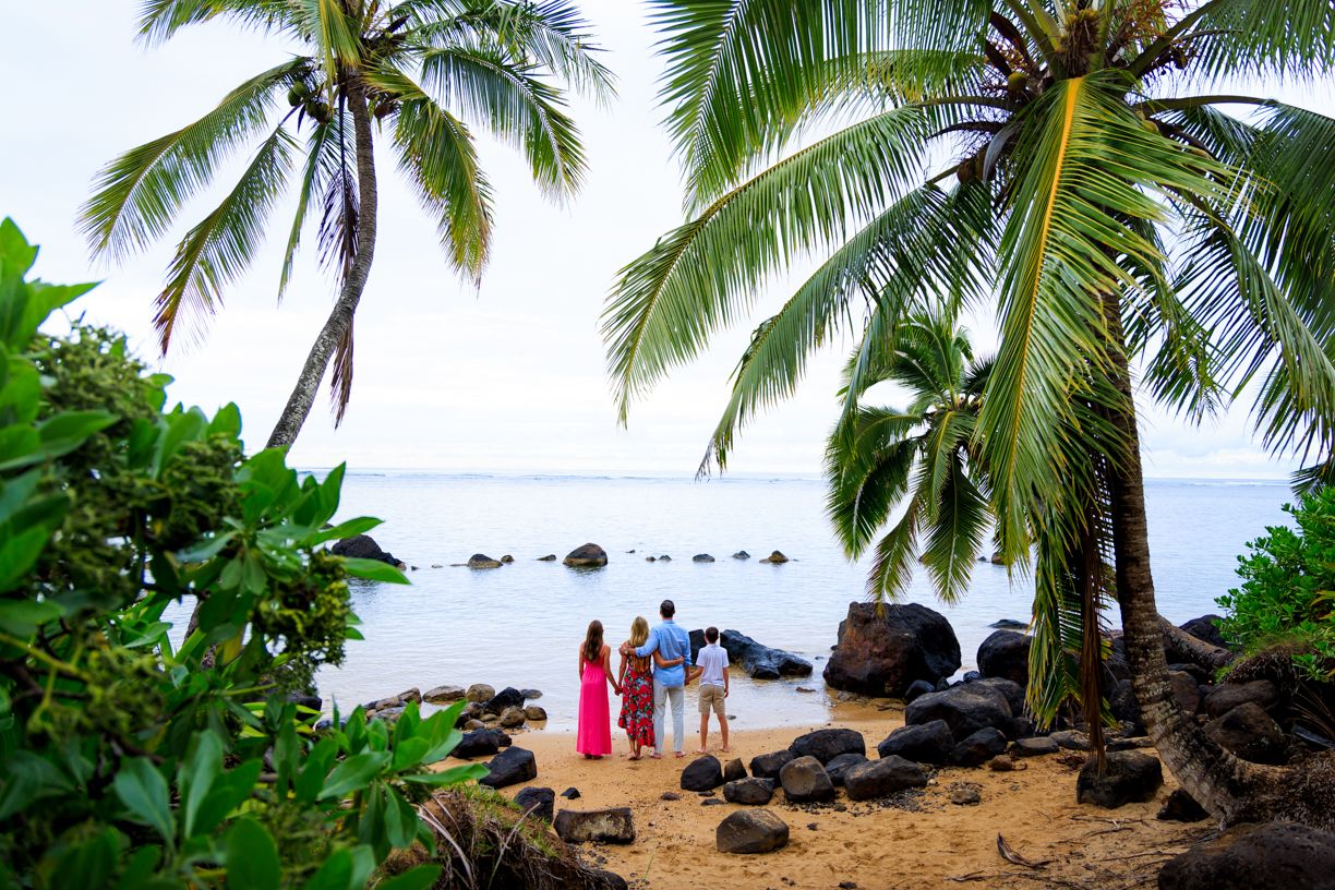 Two people walking under palm trees on tropical beach with ocean view.