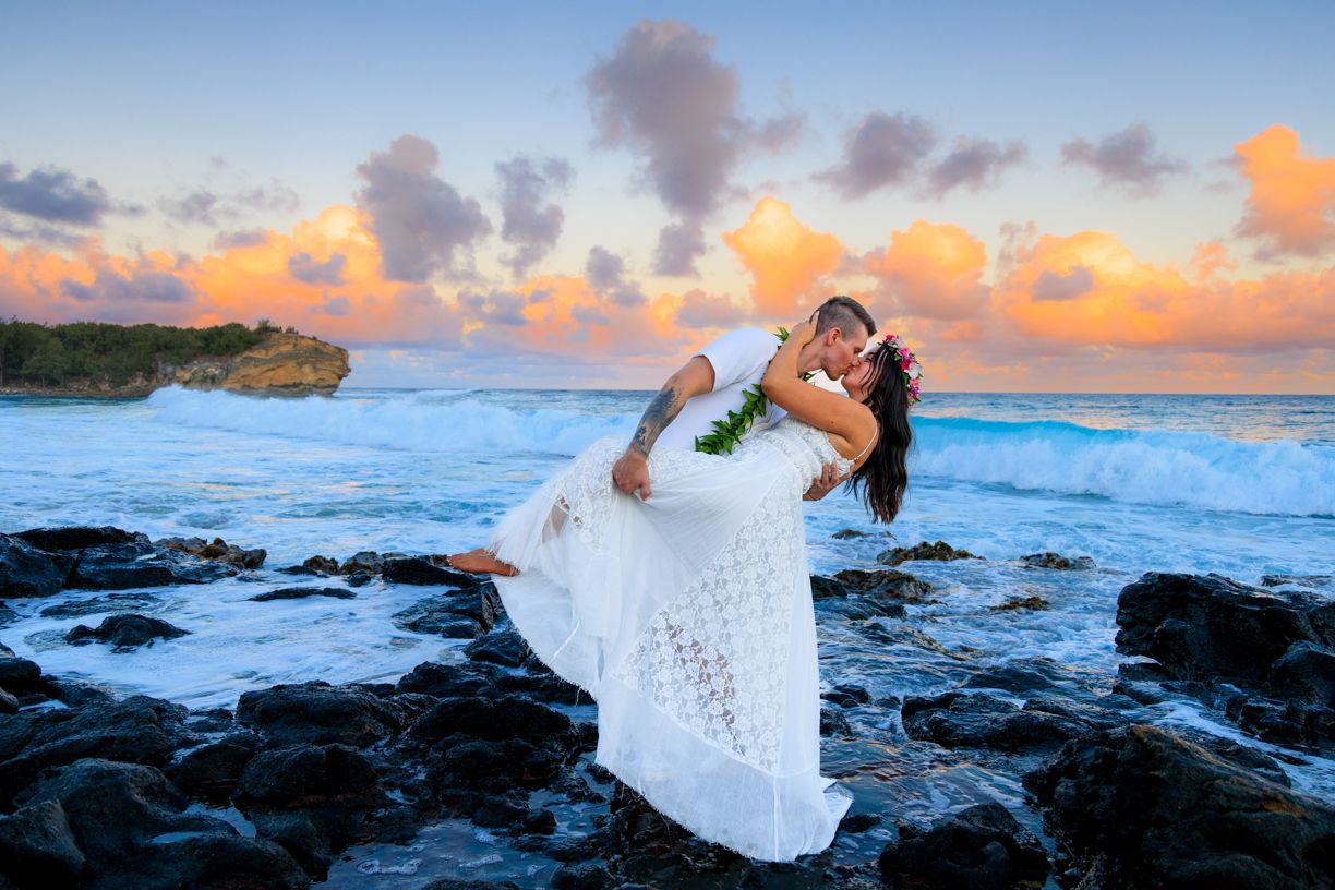 Dramatic beach photoshoot at sunset with crashing waves against black volcanic rocks.