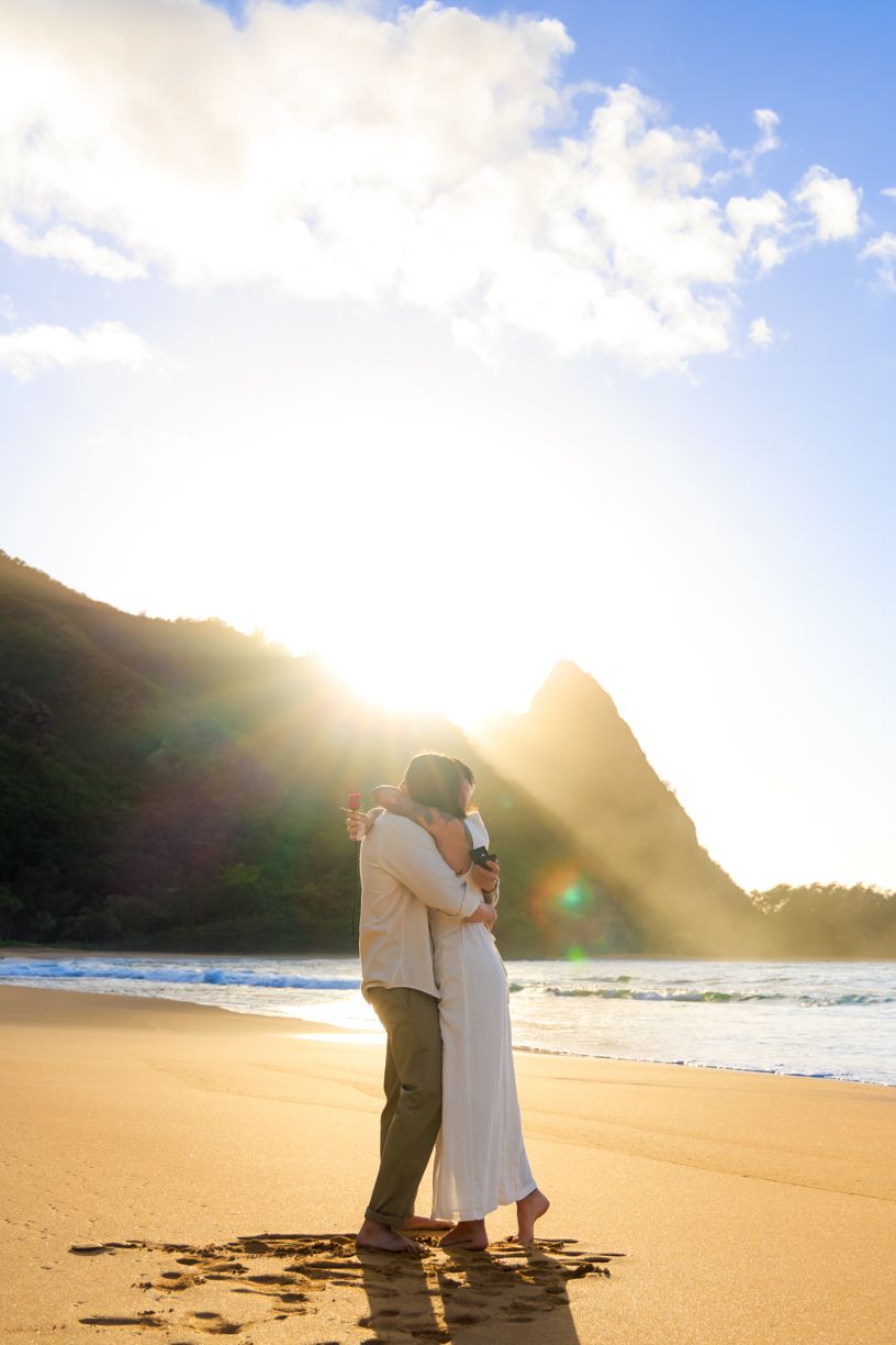 A romantic proposal scene unfolds on a golden beach at sunset with mountains in the background.