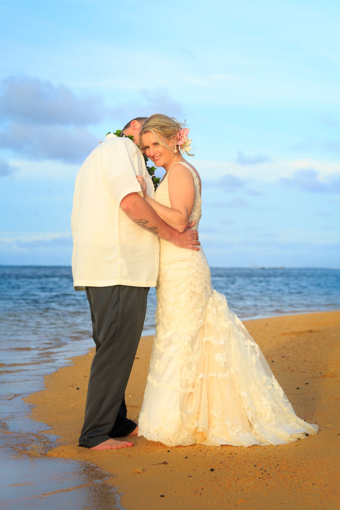 A tender moment between newlyweds on a beach at dusk.