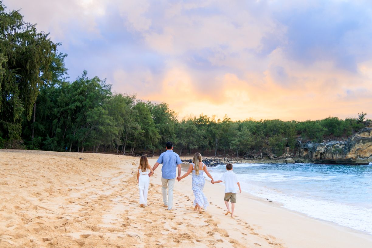 Group walking along scenic Hawaiian beach at sunset with mountains in background.