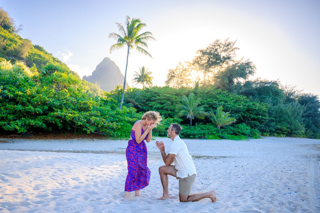 A proposal moment on a white sand beach with tropical mountain landscape.