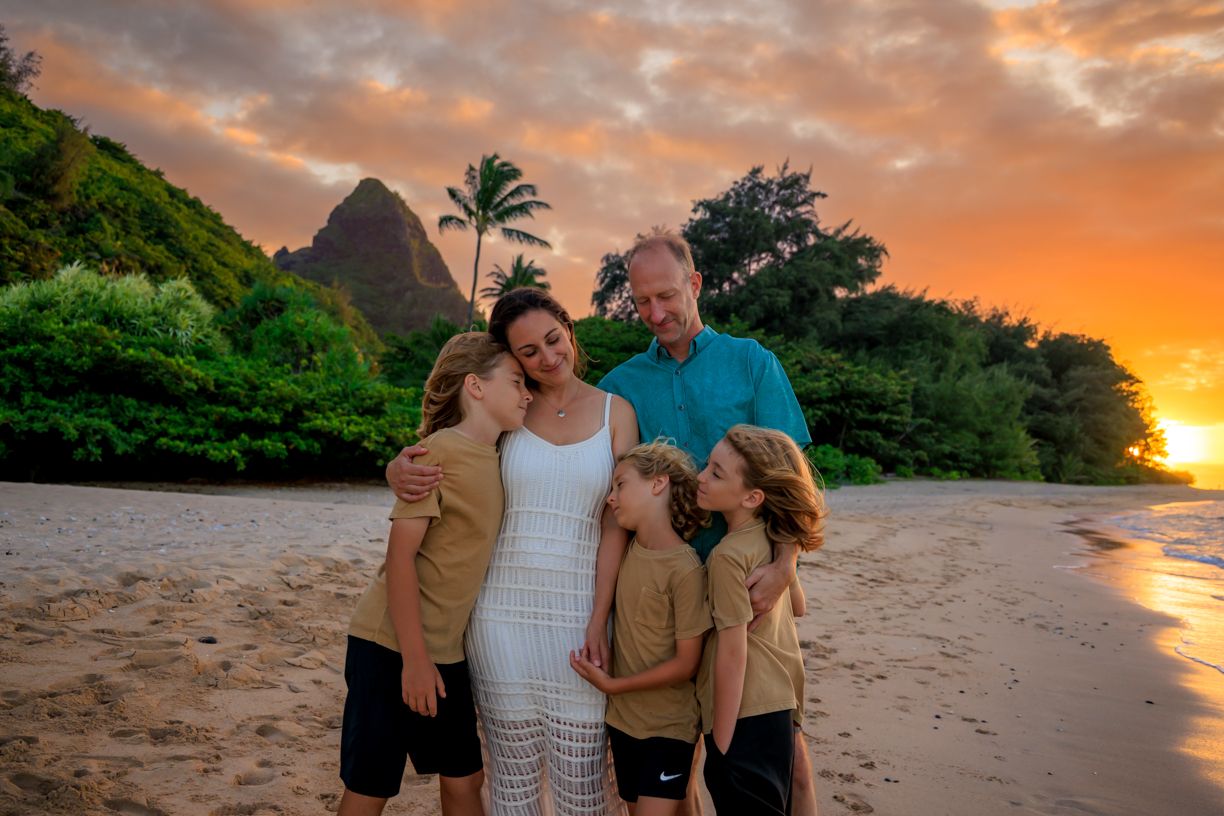 Family enjoying sunset beach walk in Hawaii with mountains and palm trees.