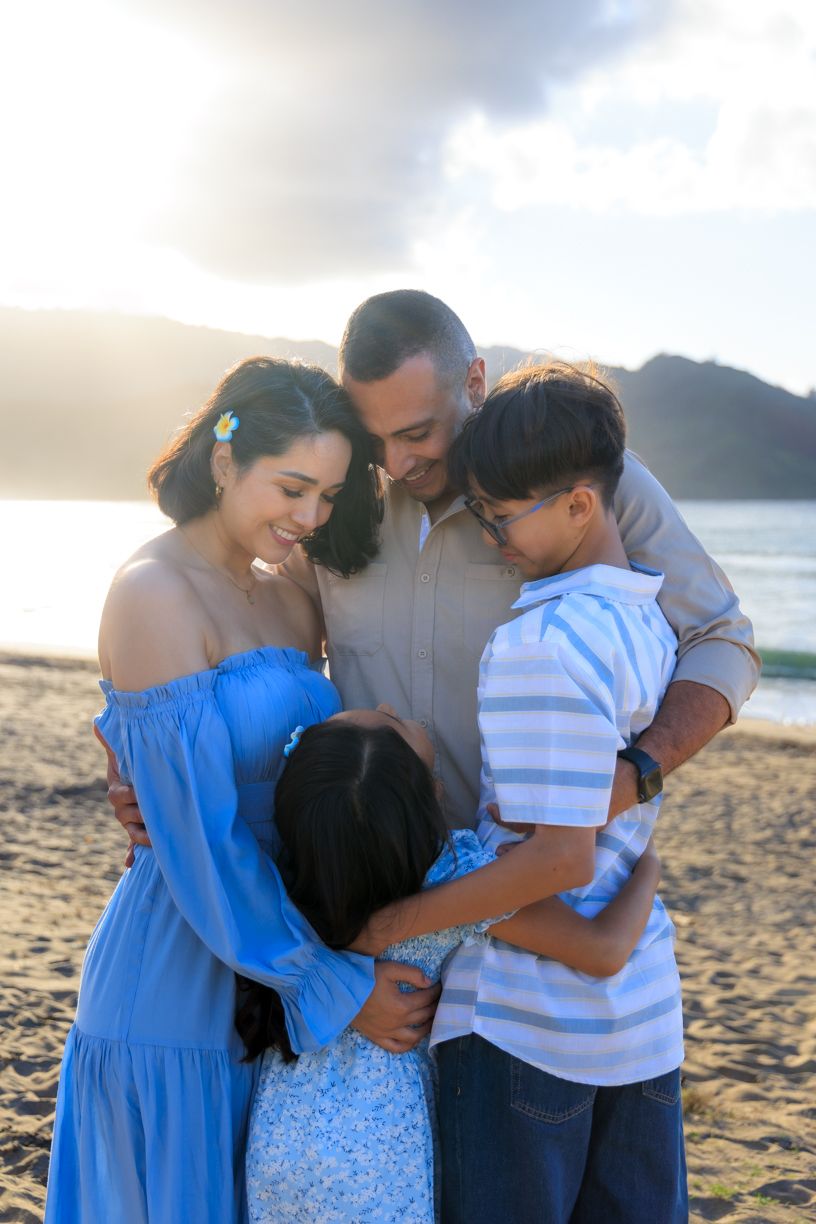 Intimate family moment captured on beach wearing coordinated blue and white outfits.