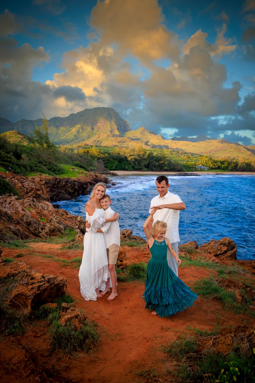 Dramatic coastal photoshoot at sunset with red cliffs, blue ocean, and lush mountains in the background.