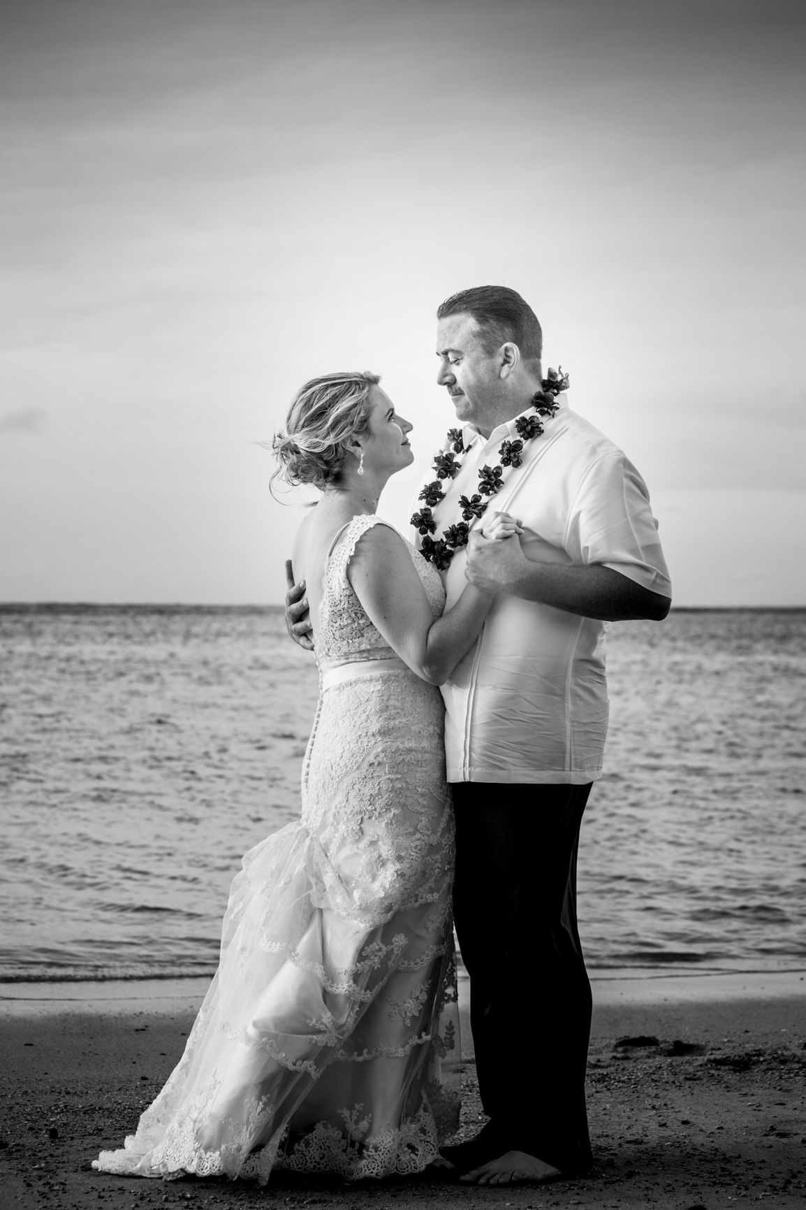 Black and white beach portrait of couple wearing traditional Hawaiian leis.