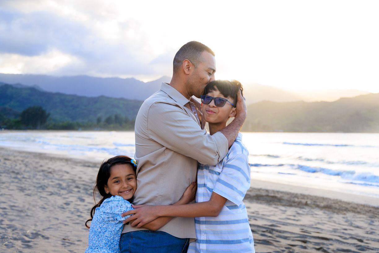 Family enjoying tender moments together on a scenic beach during golden hour.