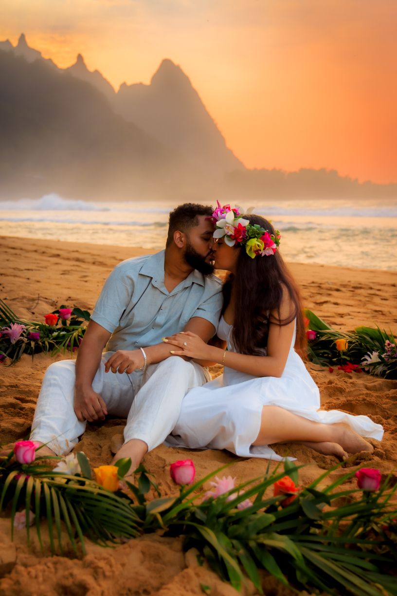 A romantic sunset beach moment surrounded by tropical flowers and palm fronds.