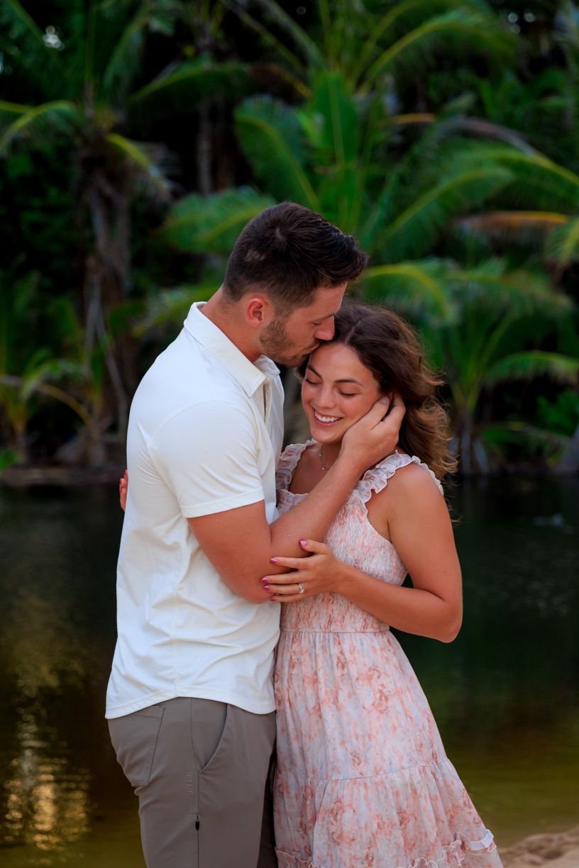 Tender moment between couple in tropical setting with palm trees.