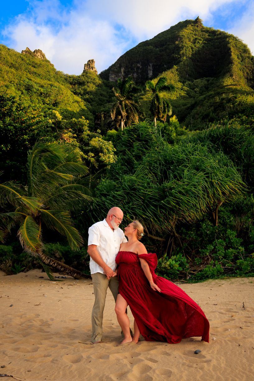 Couple embracing on sandy beach with dramatic mountain landscape in background.