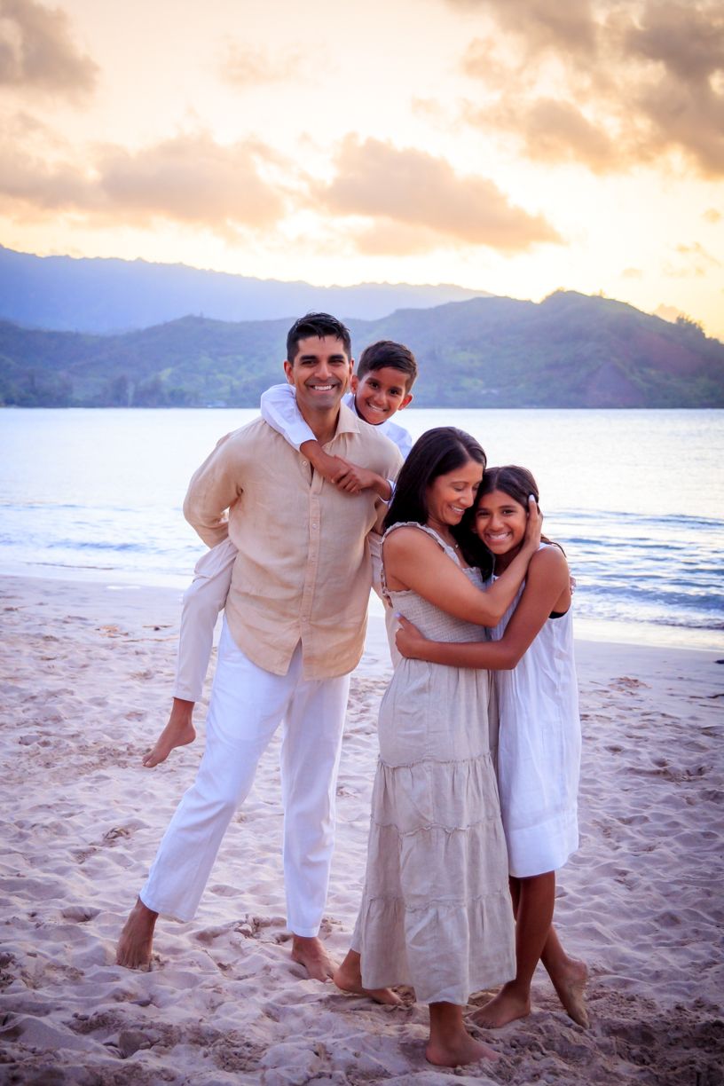 A family embracing on a beach at sunset with mountains in the background.