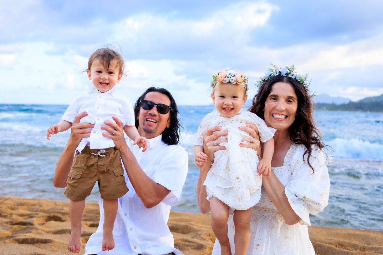 Family of four posing on beach with ocean and mountains in background.