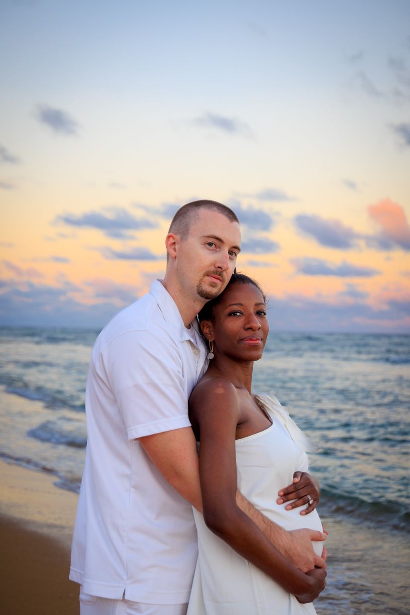 Romantic beach sunset maternity photos with couple in white attire.