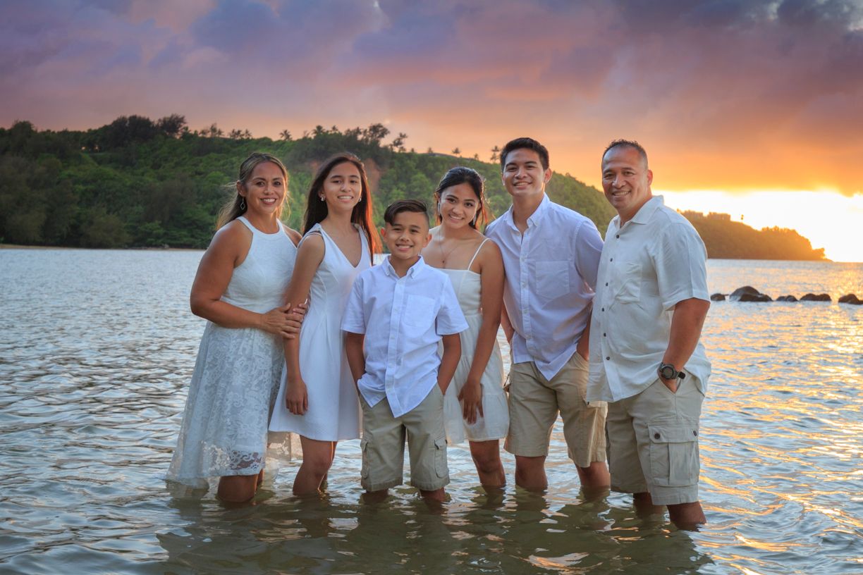 Group of six people posing in shallow water at beach during sunset.