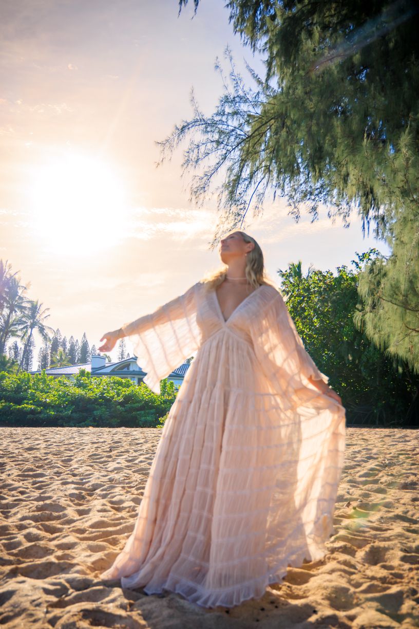 Flowing white dress catching golden sunlight on a sandy beach with palm trees at sunset.