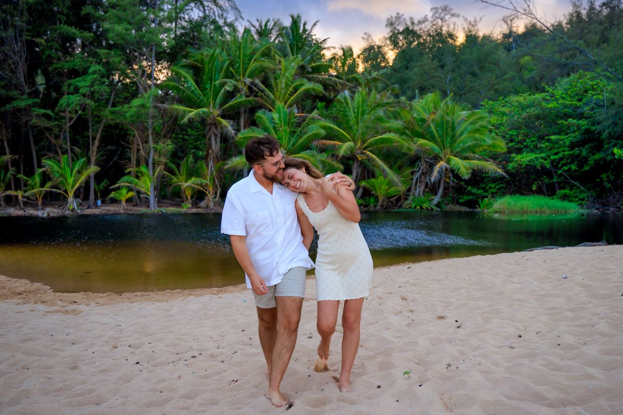 A couple embraces during a romantic photoshoot on a tropical beach with palm trees at sunset.