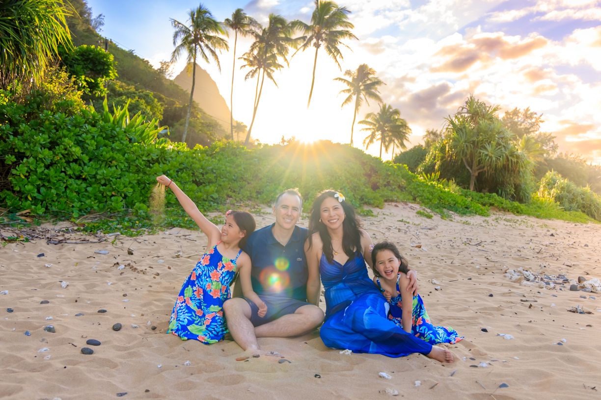 Family poses together on a tropical beach with lush palm trees and golden sunset in the background.