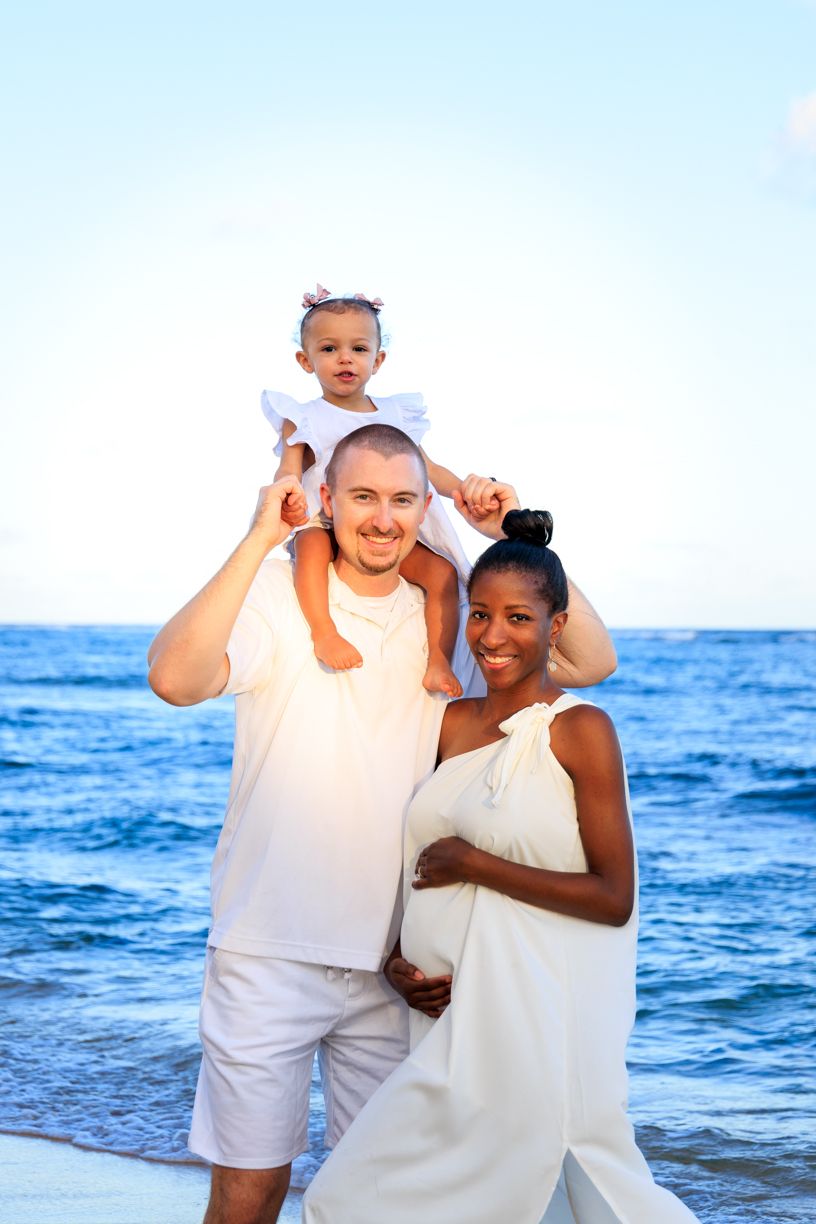 Playful family beach portraits in white clothing with ocean waves in background.