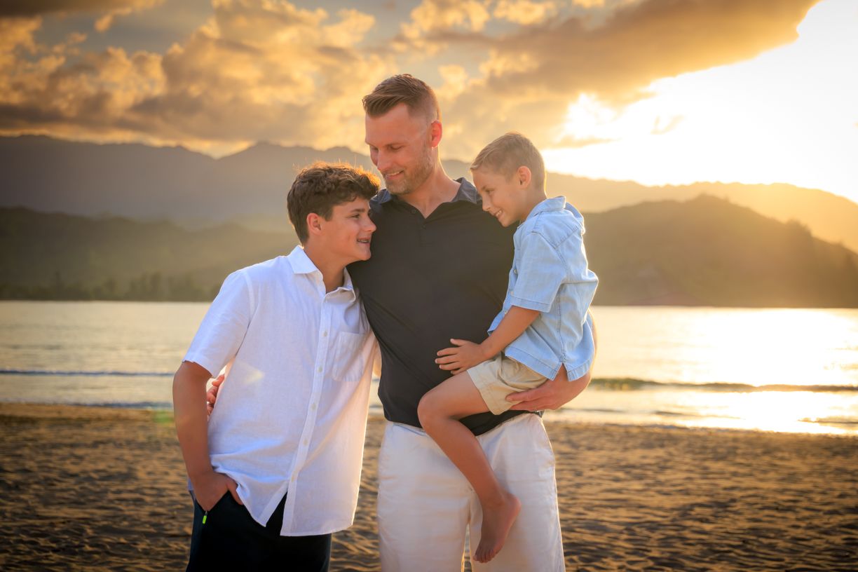 A tender family moment captured on the beach at sunset with mountains in background.
