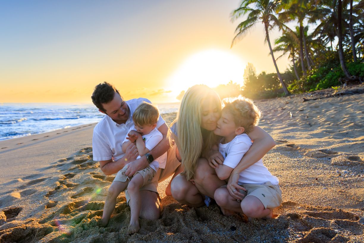 Family enjoying a peaceful sunset moment together on a sandy Hawaiian beach.
