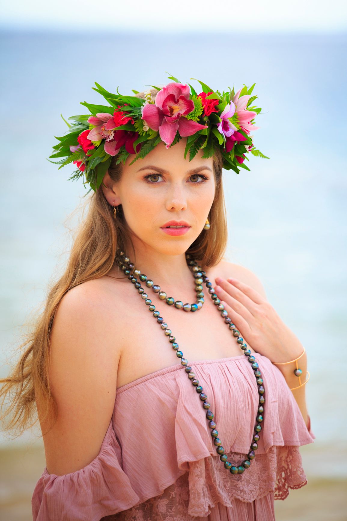 Bohemian style portrait with tropical flower crown and pink off-shoulder dress against ocean backdrop.