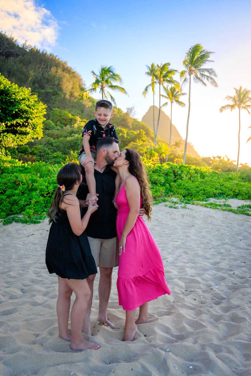 Family enjoying sunset moments together on a tropical beach with palm trees in the background.