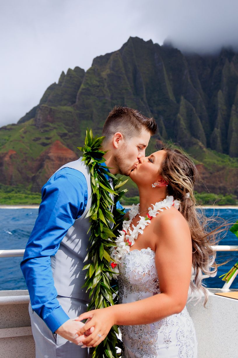 Intimate wedding ceremony aboard boat with majestic Na Pali coast mountains in background.