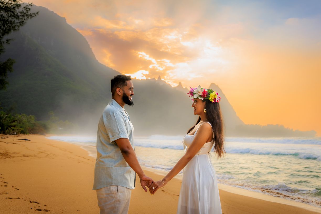 A romantic beach photoshoot during golden hour with mountains and ocean waves in the background.