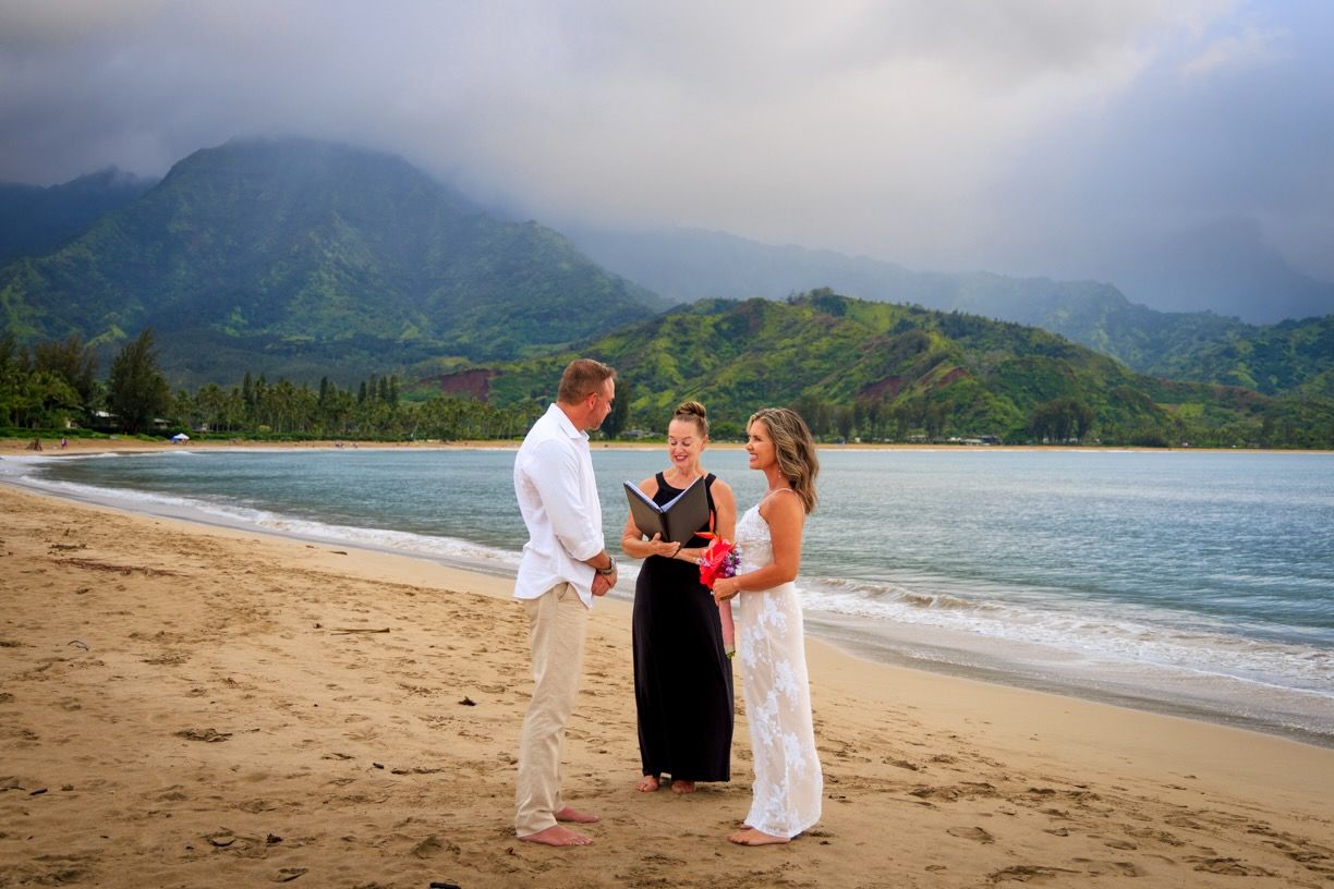 Beach wedding ceremony on Hawaiian shore with mountains and ocean backdrop.