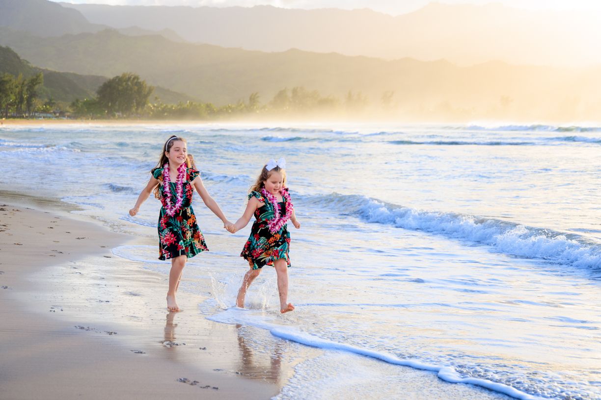 Playful beach photoshoot at sunset with waves crashing along a tropical shoreline.
