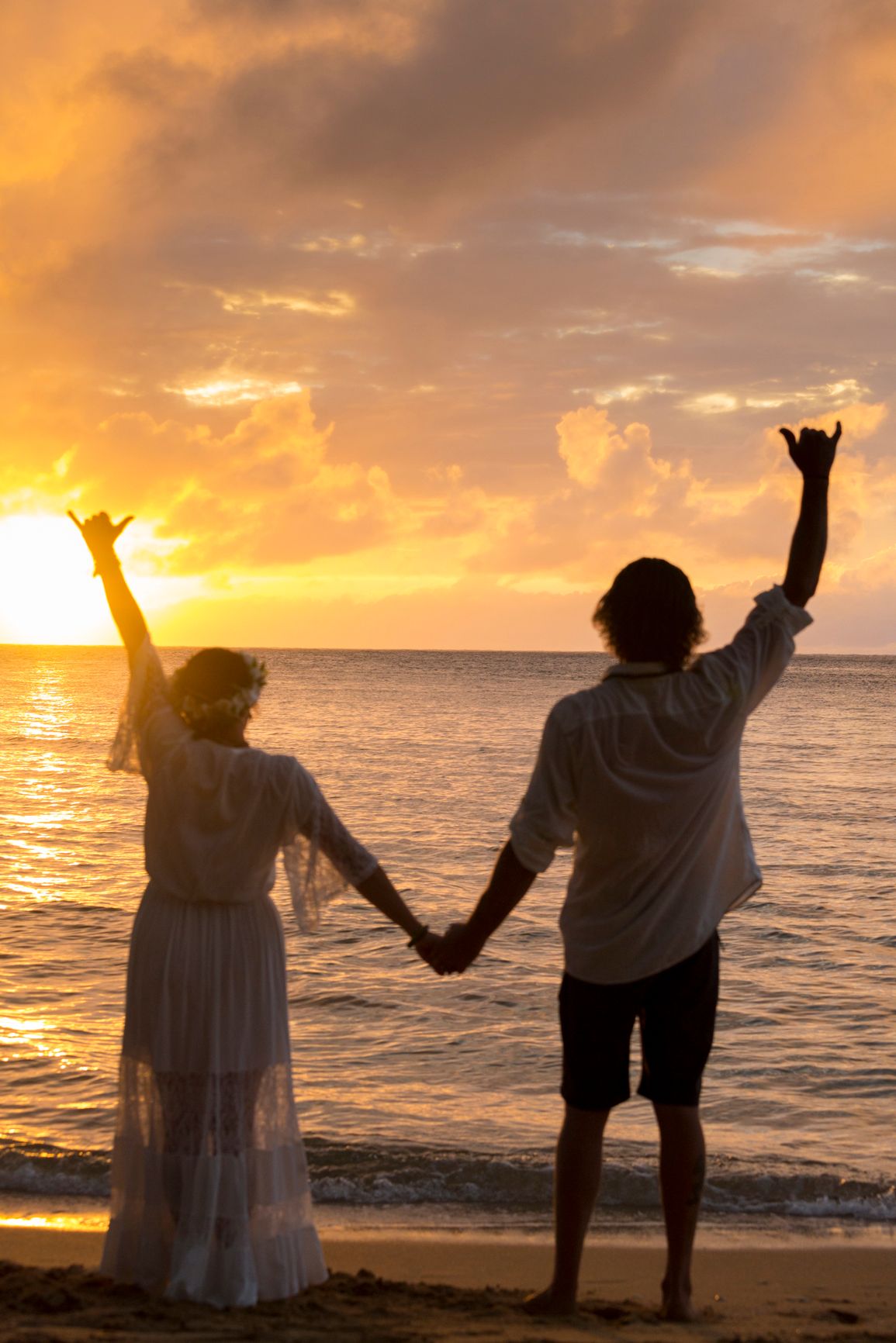 Silhouette of couple holding hands with raised arms on beach at sunset.