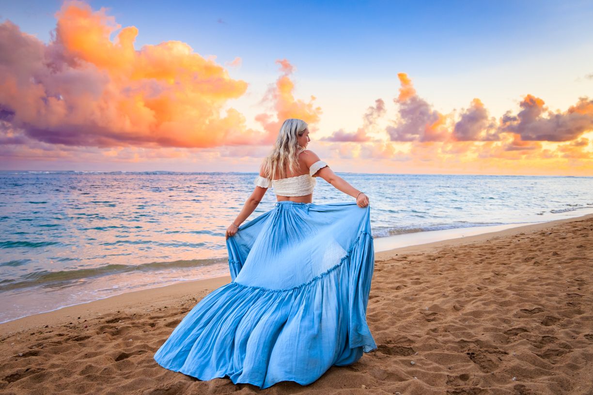 Turquoise dress flowing in ocean breeze during vibrant beach sunset.