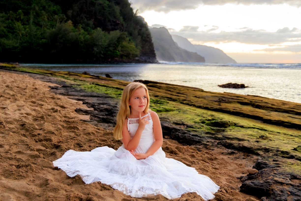 Coastal photography session with white dress against dramatic cliff and ocean backdrop at sunset.