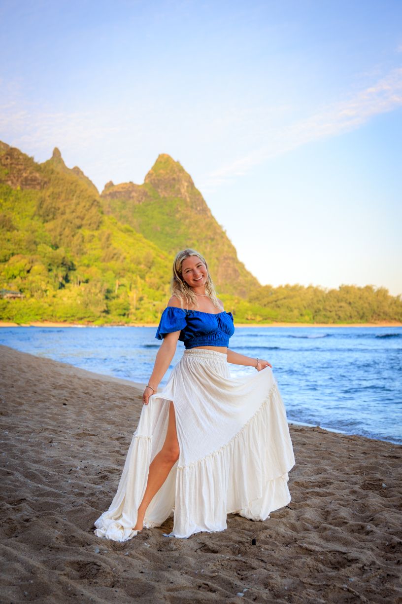 White flowing maxi dress with blue top photographed on black sand beach with mountain backdrop.