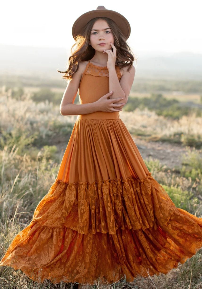 Rust-colored tiered maxi dress with lace details photographed in golden field at sunset.