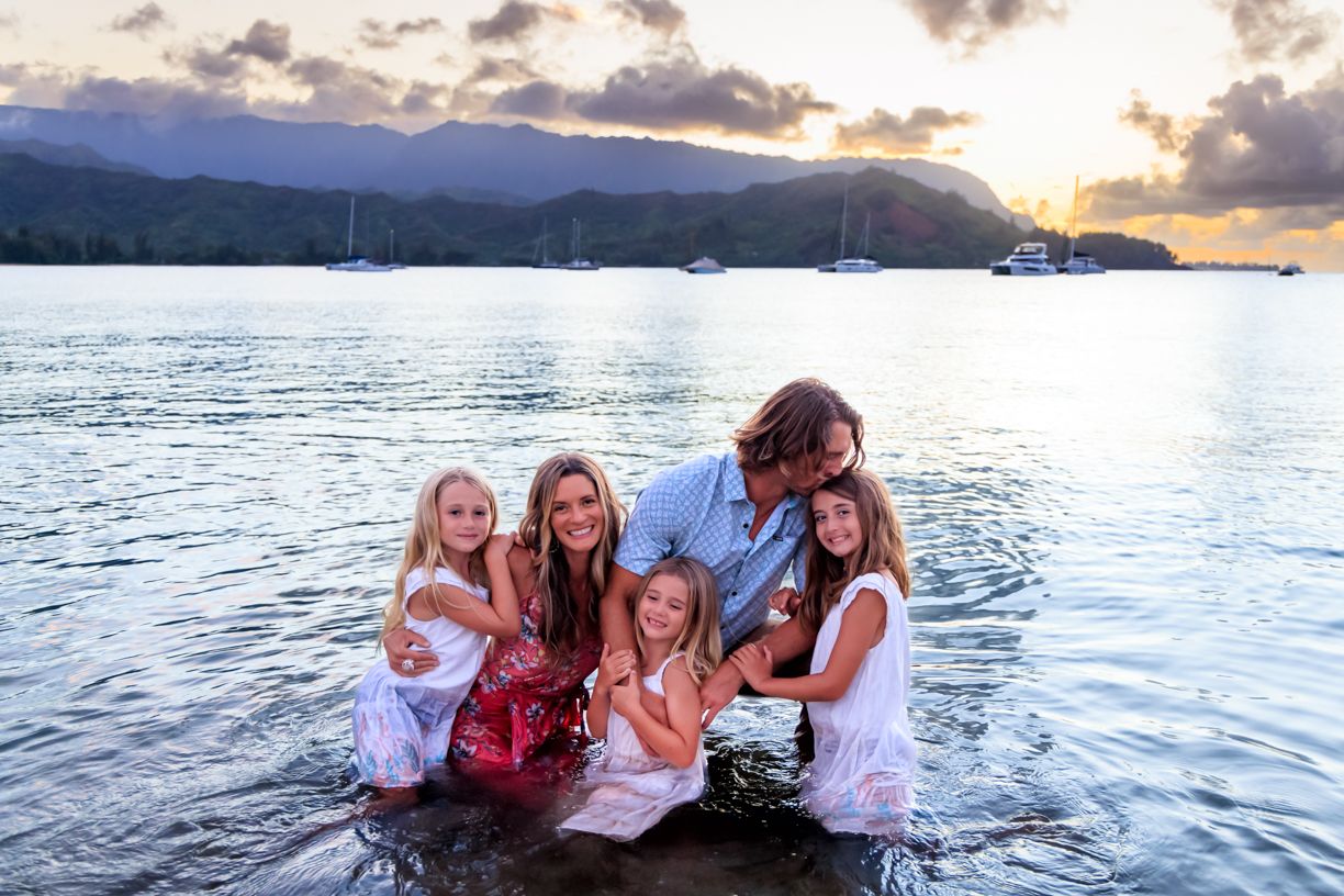 Group enjoying sunset together in ocean water with mountains and boats in background.