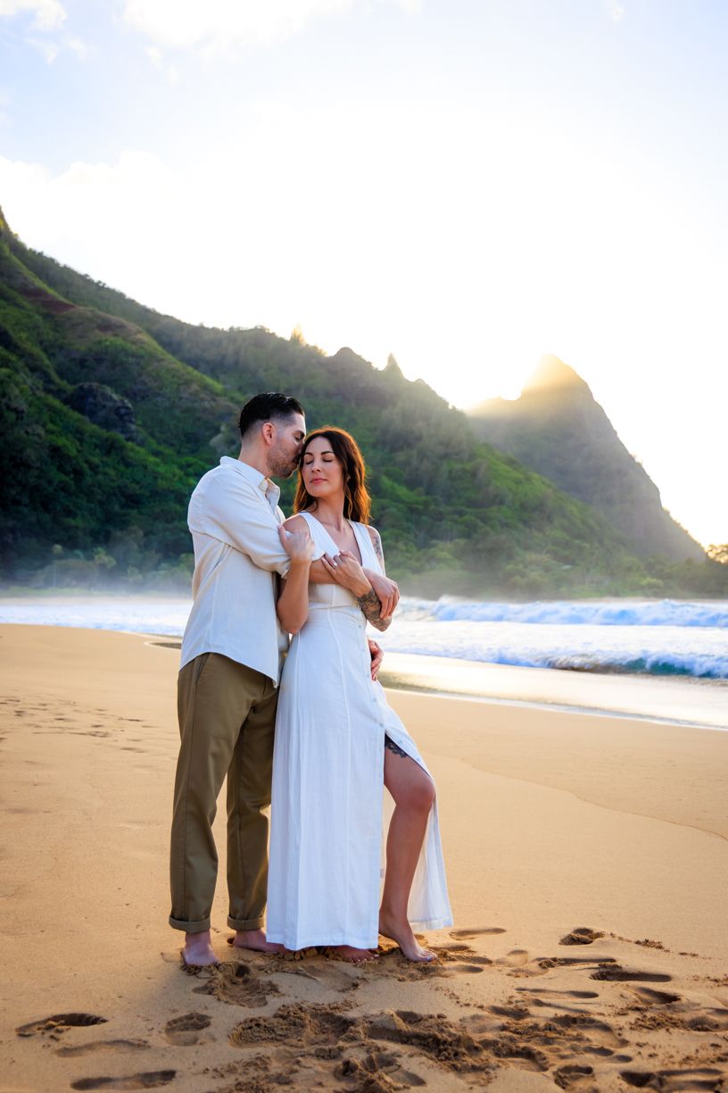 Romantic beach photoshoot with dramatic mountain backdrop at sunset.