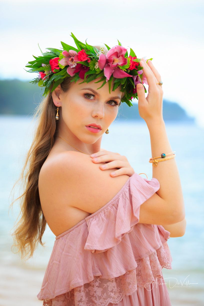 Tropical beach photoshoot featuring pink floral crown and ruffled dress against ocean backdrop.