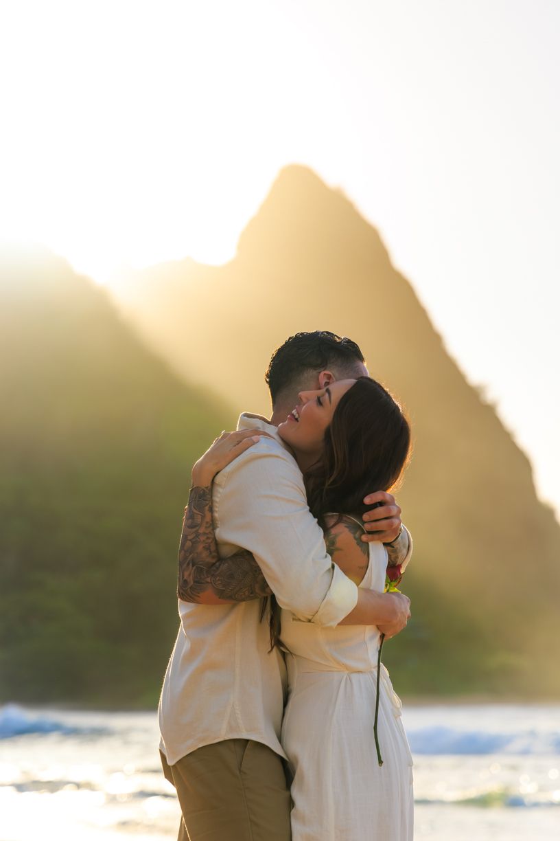 Romantic couple embracing on a beach at sunset with mountains in the background.