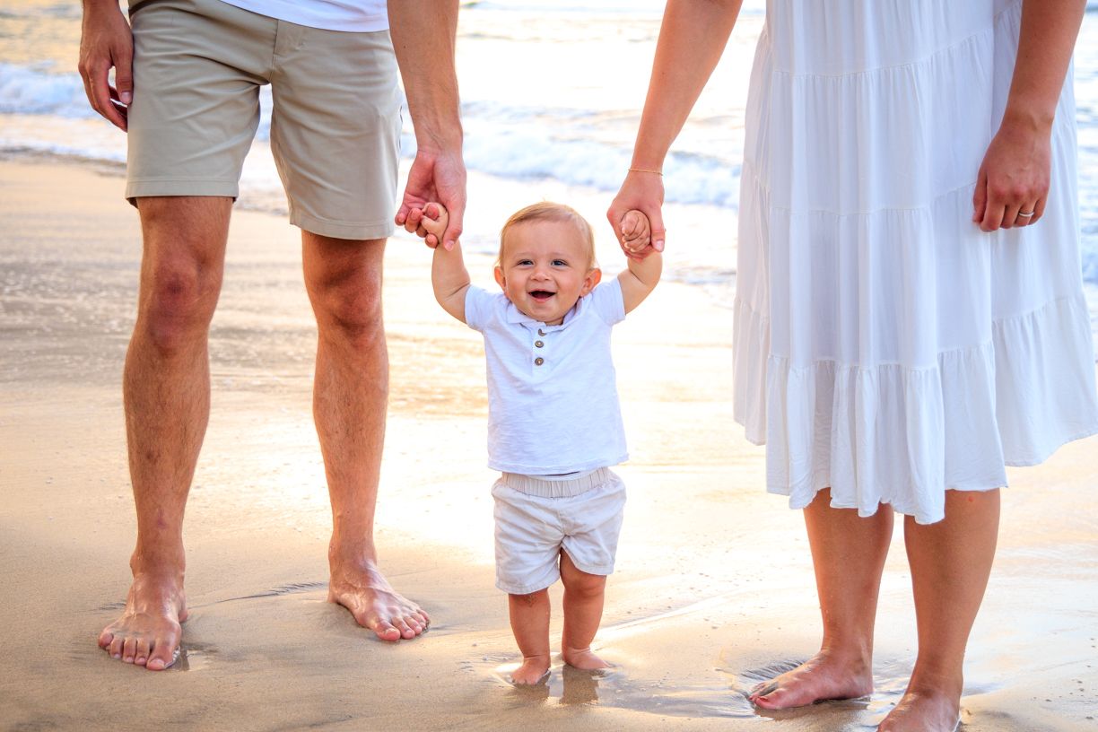 Bare feet of family members standing together on wet sand at the beach.