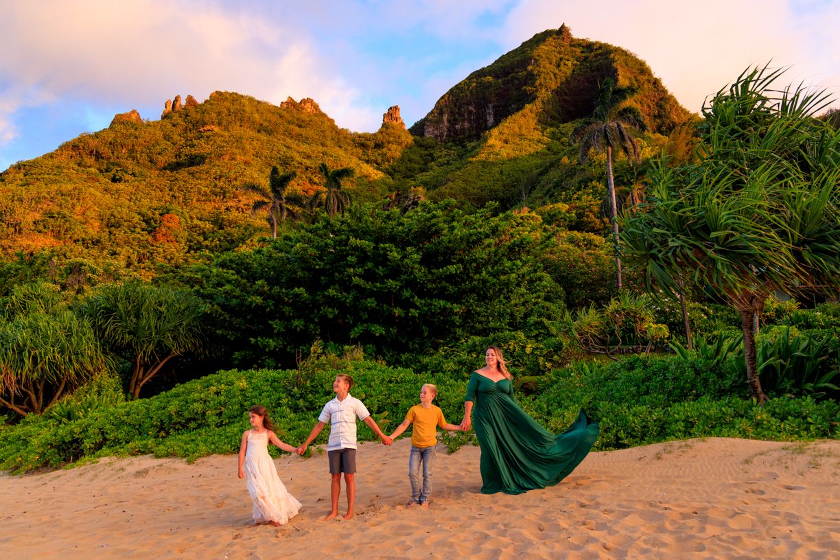 Family walks along scenic tropical beach path at sunset with mountains in background.