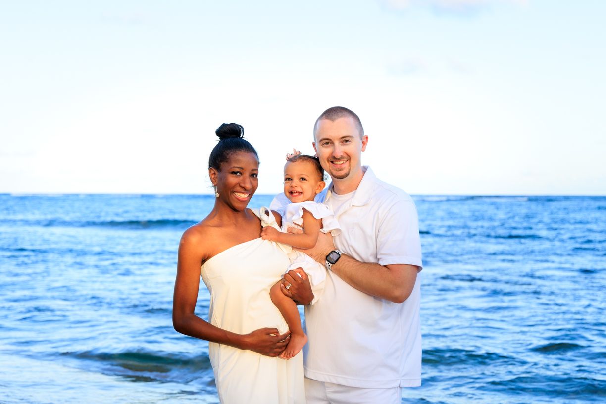 Family beach photoshoot with white outfits against ocean backdrop.