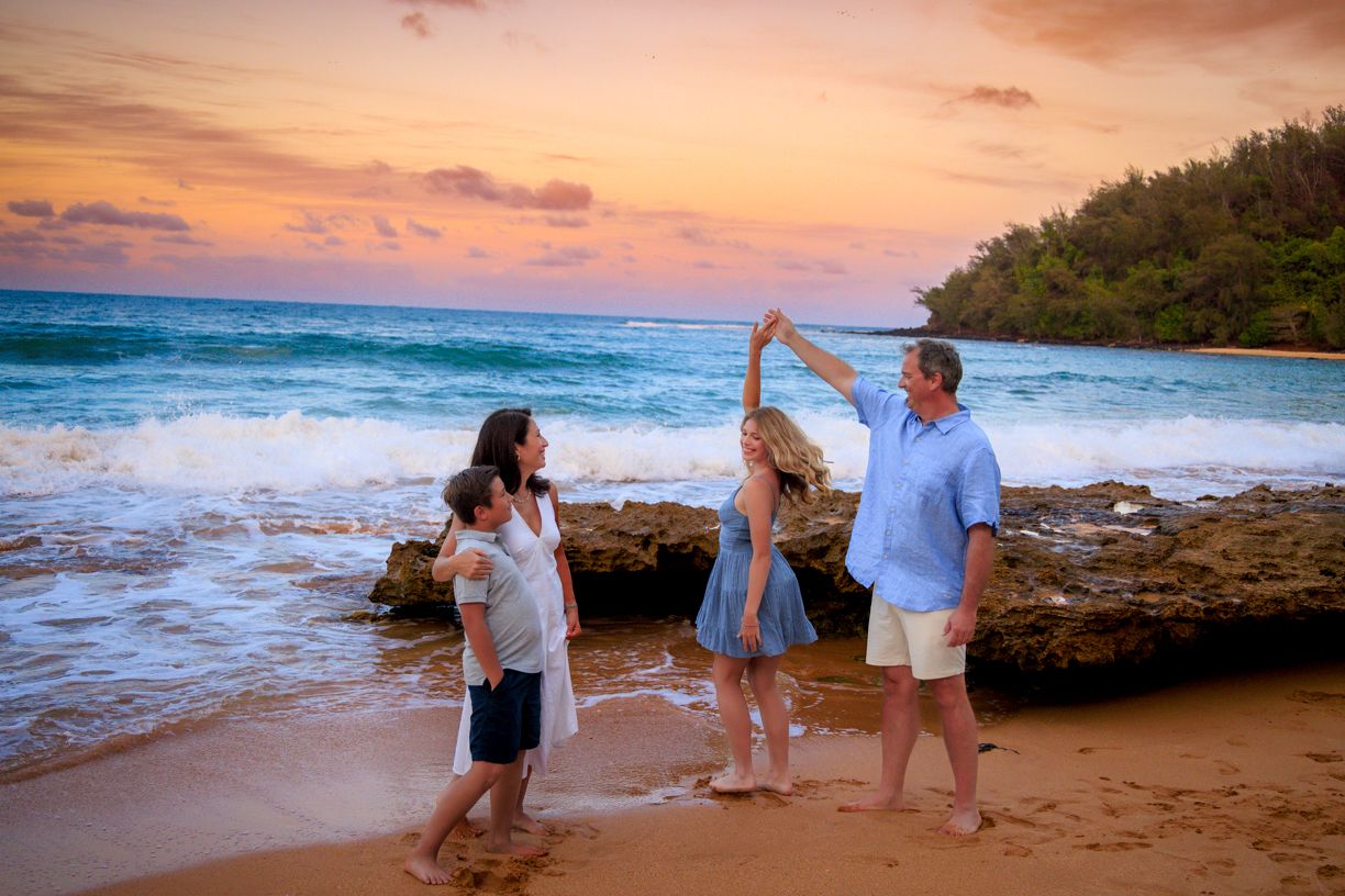Family playing and posing together on a sandy beach during a vibrant orange sunset.