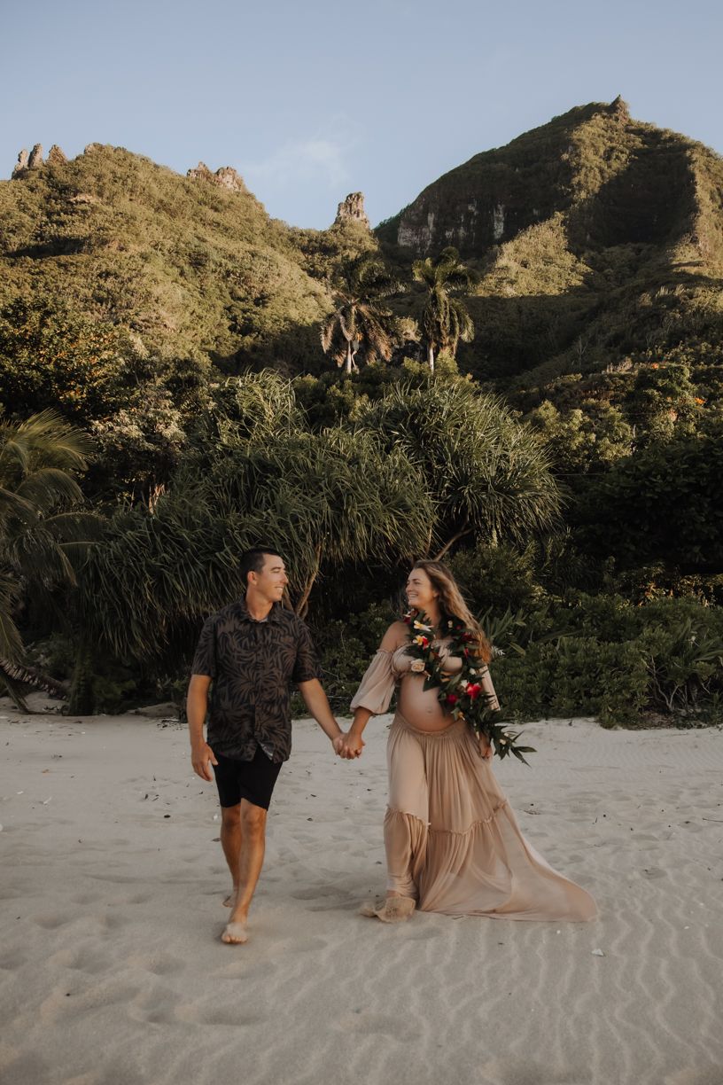 Maternity photoshoot on sandy beach with mountainous backdrop at golden hour.