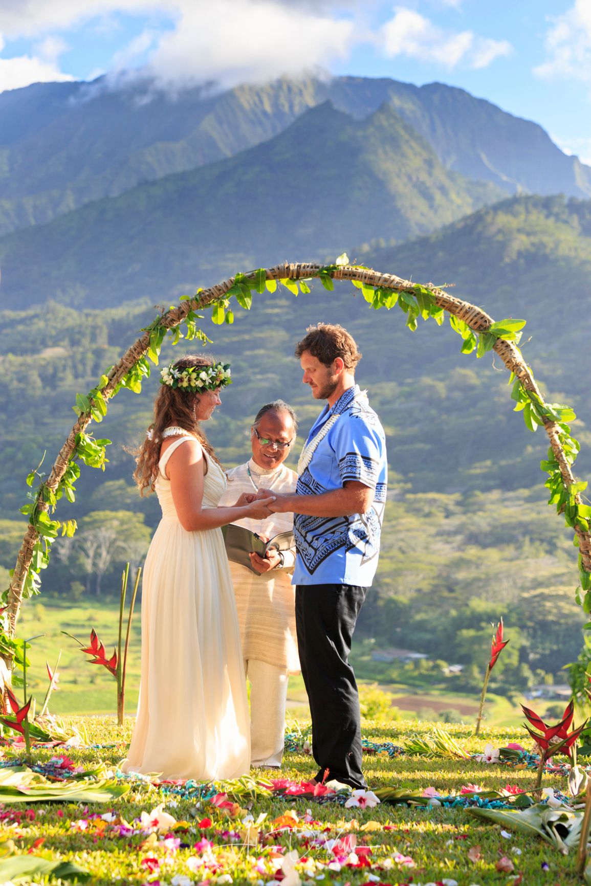 Wedding ceremony under a floral arch with mountain views in Hawaii.