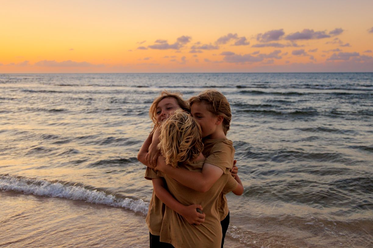 Couple embracing on beach at sunset with ocean waves in background.