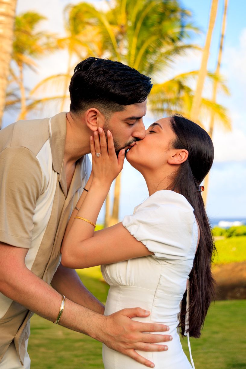 A romantic couple sharing intimate kisses with palm trees and ocean in the background.